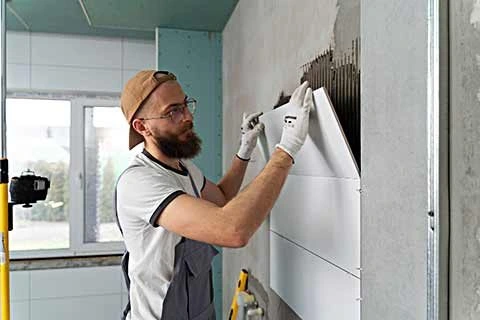 Worker installing white wall tiles using adhesive during a bathroom or kitchen renovation.