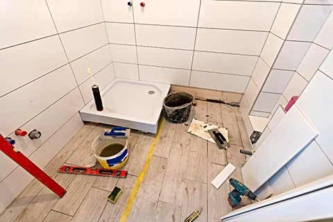 Bathroom renovation in progress with wall tiles, floor tiles, shower tray, and tools scattered on the floor.