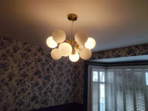 Modern gold chandelier ceiling light with floral wallpaper and navy painted walls in London home