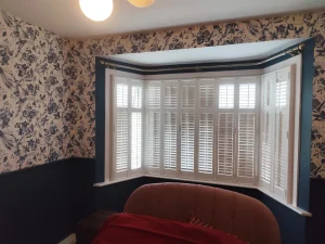 Bay window with white plantation shutters and navy painted wall in London room